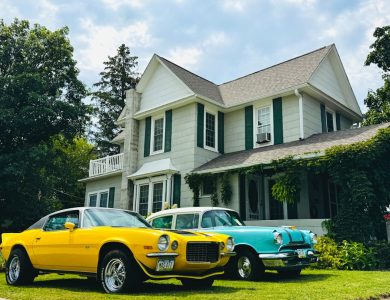 Two vintage cars parked in front of a large house.